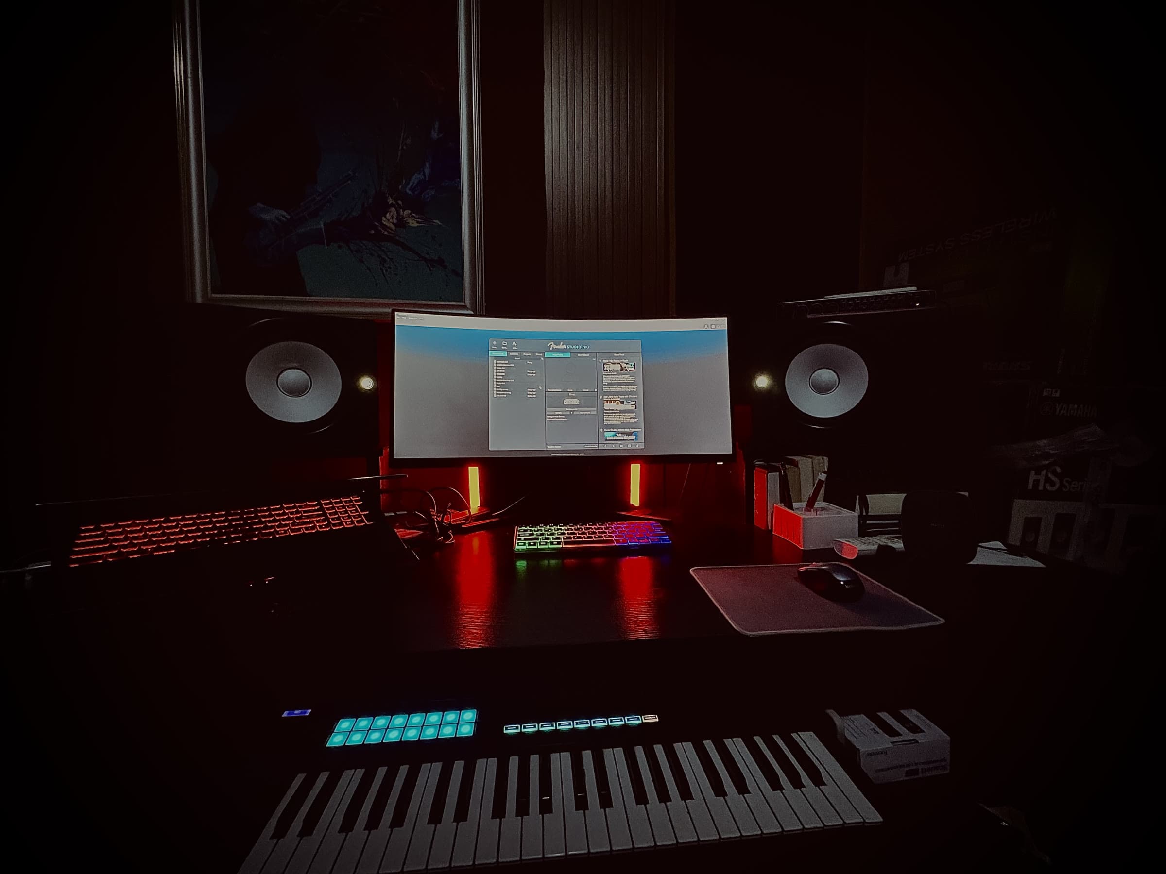 The studio's digital production desk — dual monitors, MIDI keyboard, and pad controller lit in red